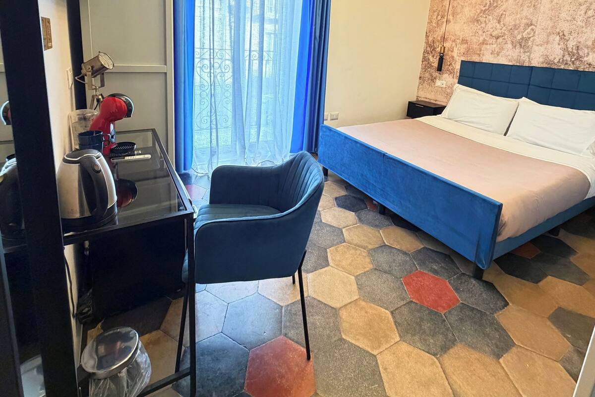 Une chambre d’hôtel équipée d’un lit, d’un bureau, d’une chaise, d’une machine à café et d’une fenêtre avec des rideaux.