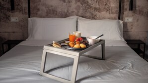 A neatly made bed with a tray of breakfast items including toast, fruit, and a beverage, set against a textured wall with a modern light fixture. - Dimora San Lorenzo (Taranto)