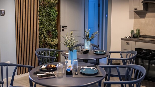 A modern dining area with round tables and blue chairs, a small kitchen with a stove, and a vertical garden wall. - Dimora San Lorenzo (Taranto)