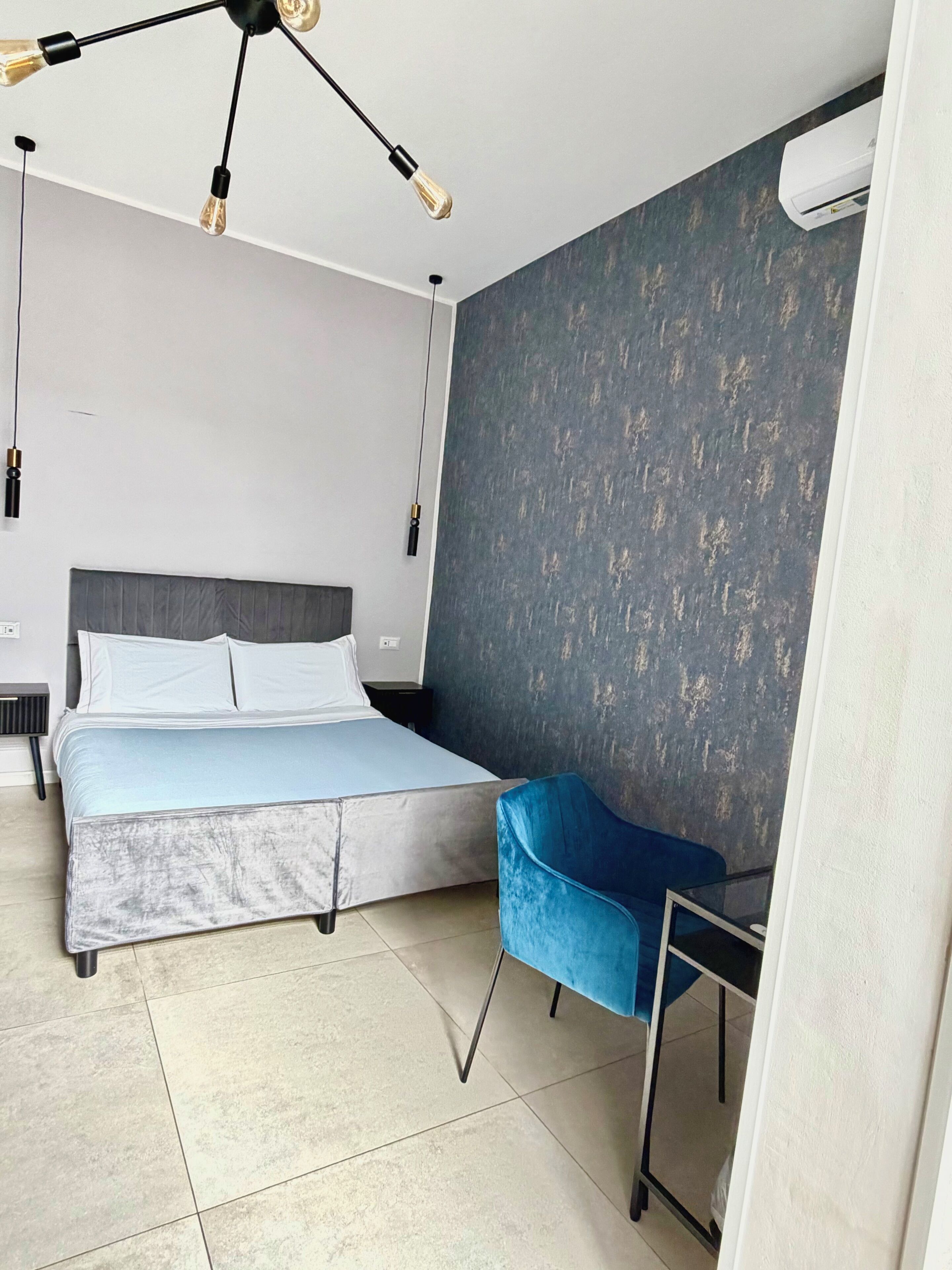Un dormitorio con una cama, una silla azul, un escritorio y una lámpara en el techo.