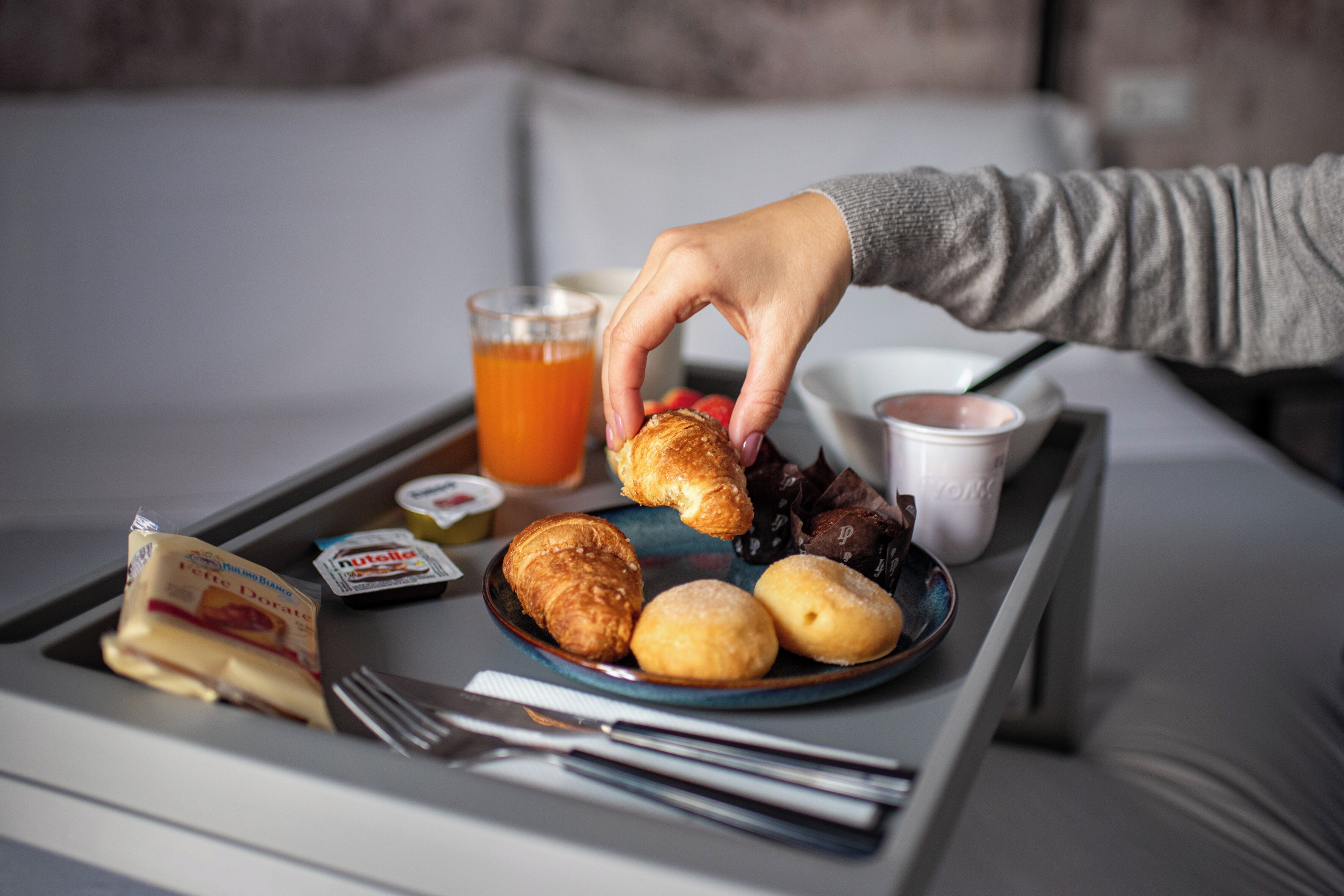 Una bandeja con cruasanes, un vaso de jugo de naranja, un pequeño recipiente de Nutella y una porción de mantequilla.