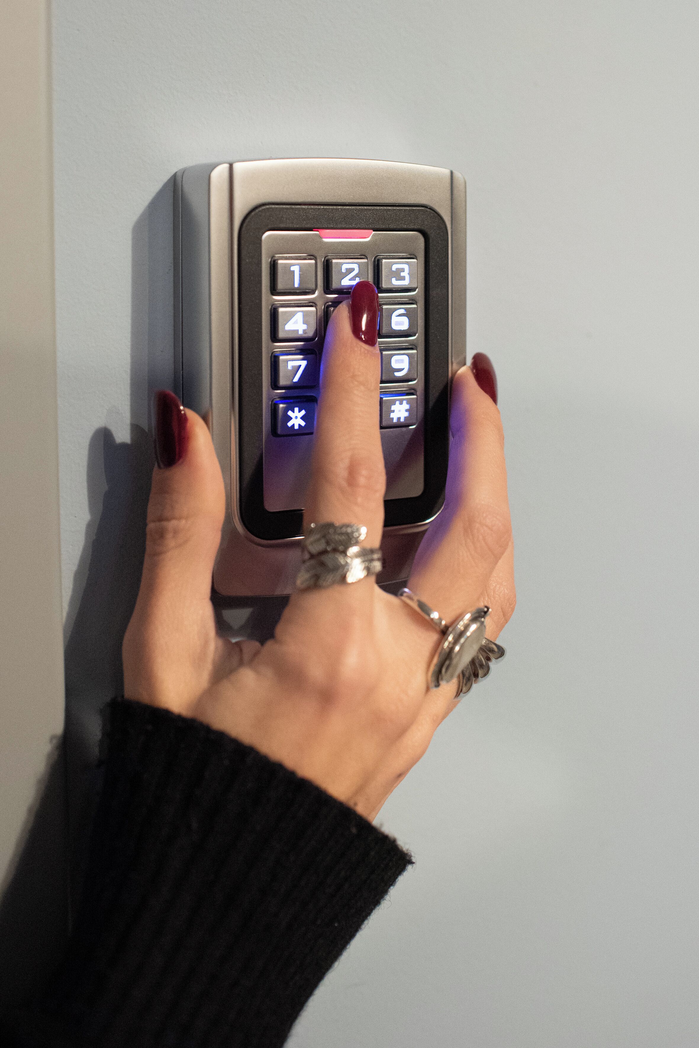 A hand pressing a numeric keypad on a door lock.