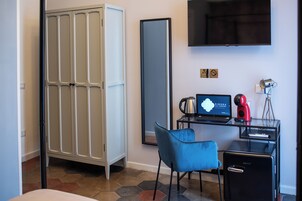 Habitación de hotel con armario, escritorio con laptop, silla, cafetera y televisión.