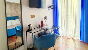 A hotel room with a bed, a desk with a chair, a television, and a window with blue curtains. - Dimora San Lorenzo (Taranto)
