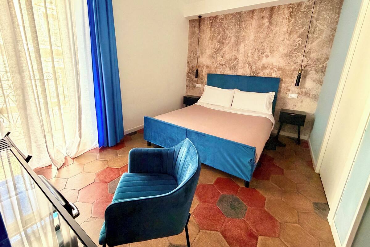 Une chambre à coucher comprenant un lit, une chaise, une table de chevet et un mur orné d’un motif texturé.