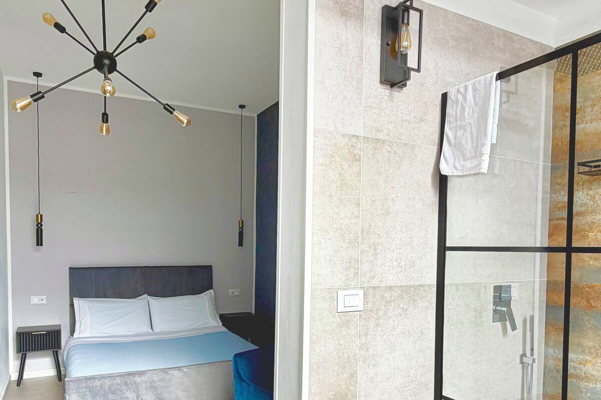 Une chambre moderne avec un lit, un luminaire suspendu et un espace douche doté d’une porte en verre.