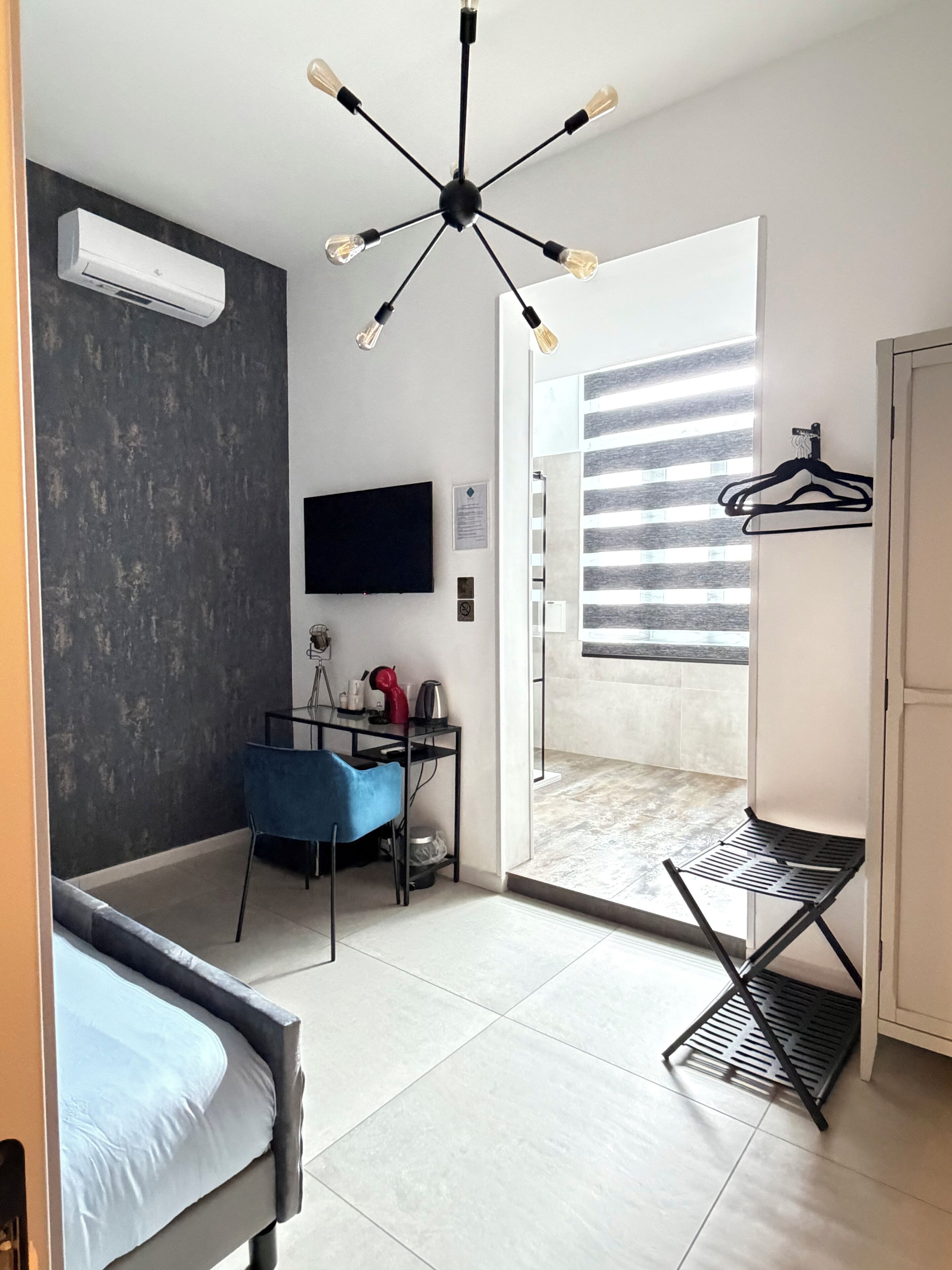 A modern bedroom with a bed, a desk, a chair, a TV, and a ceiling light fixture.
