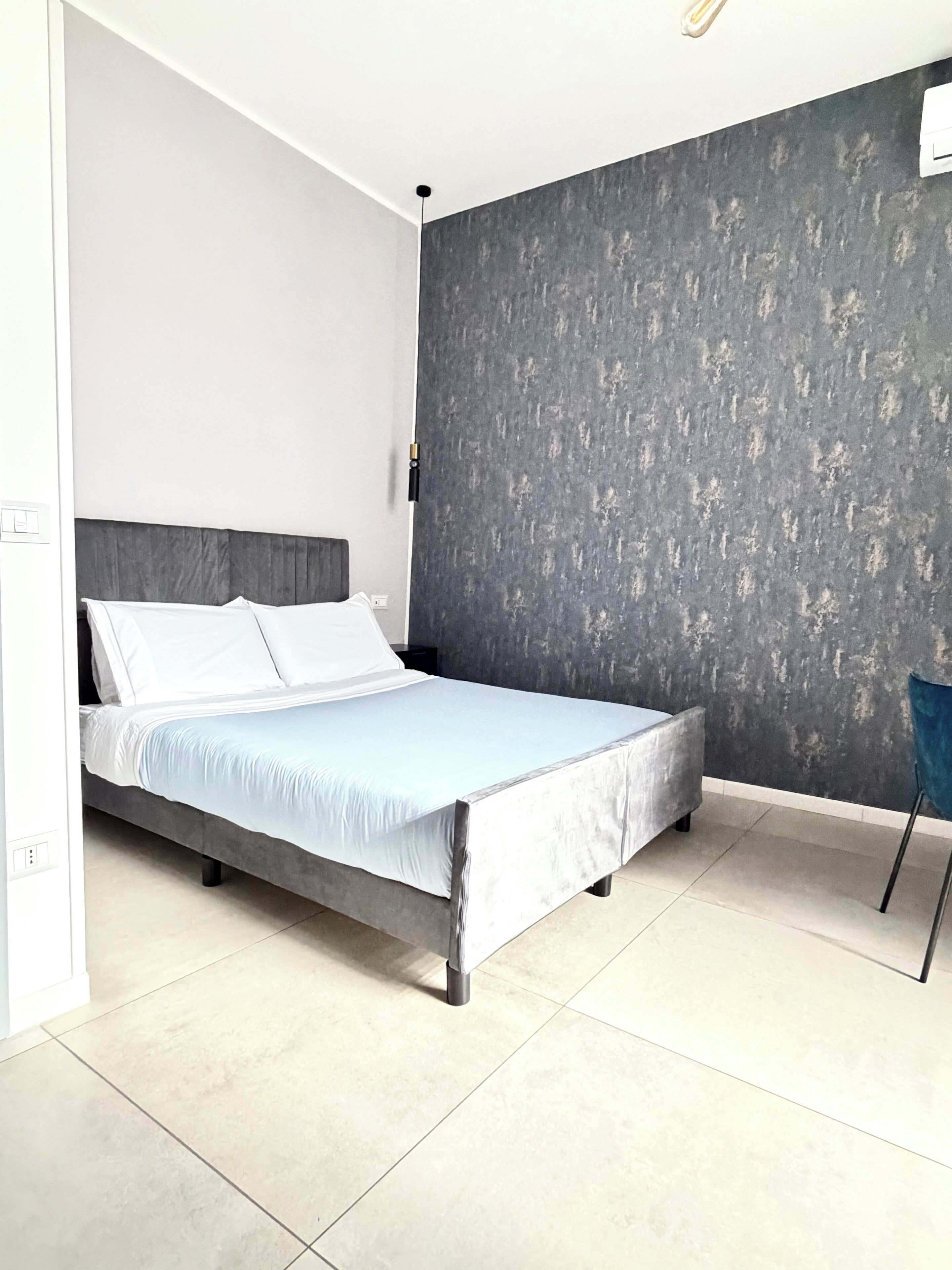 A modern bedroom with a bed, a grey textured wall, and a white ceiling.