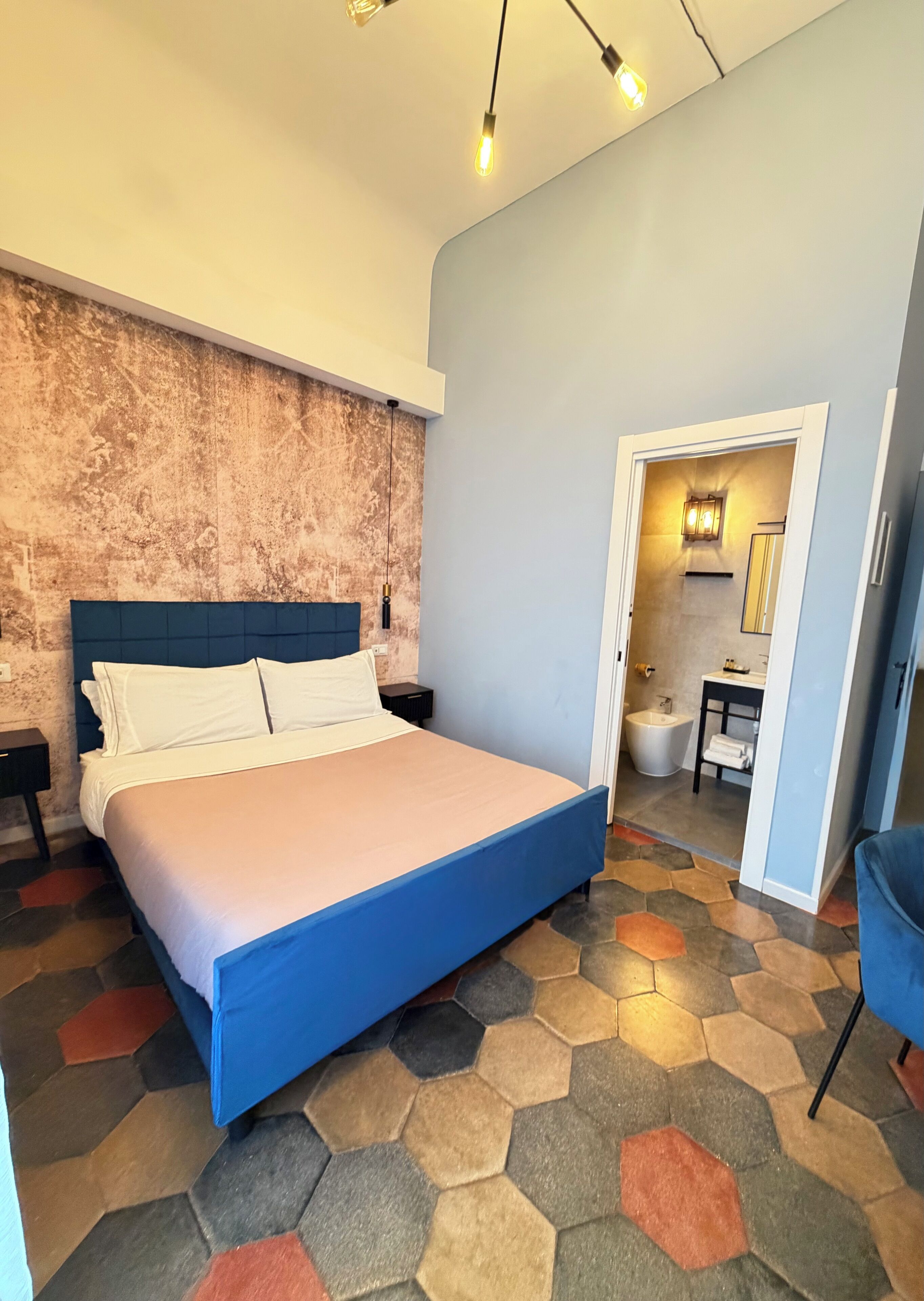 A modern bedroom with a large bed, a textured wall, and a hexagonal patterned floor.