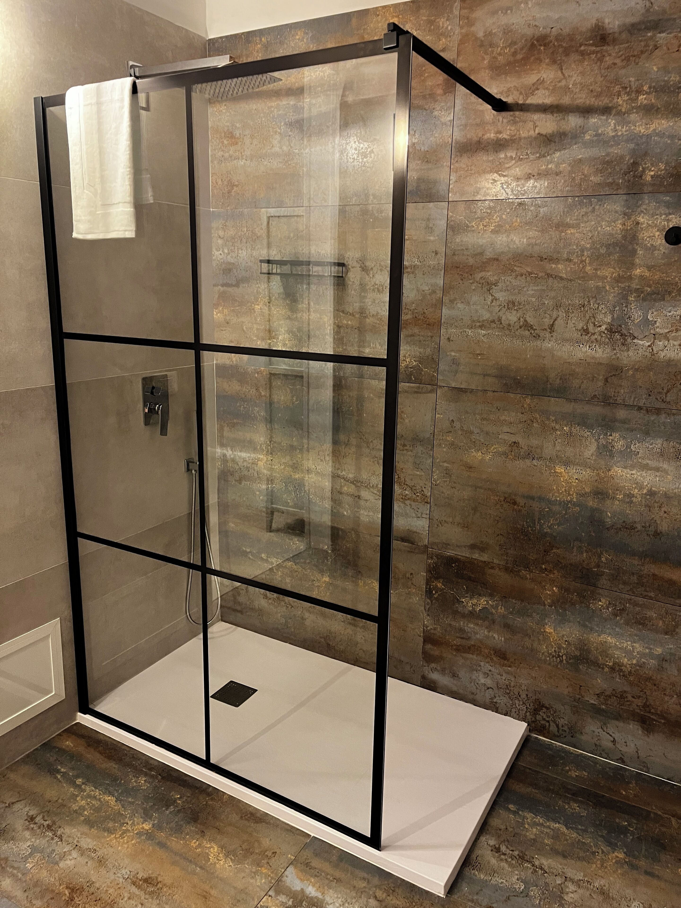 Une douche entièrementClose avec des parois en verre, un sol blanc et un mur texturé à l’arrière.