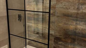 Une douche entièrementClose avec des parois en verre, un sol blanc et un mur texturé à l’arrière.