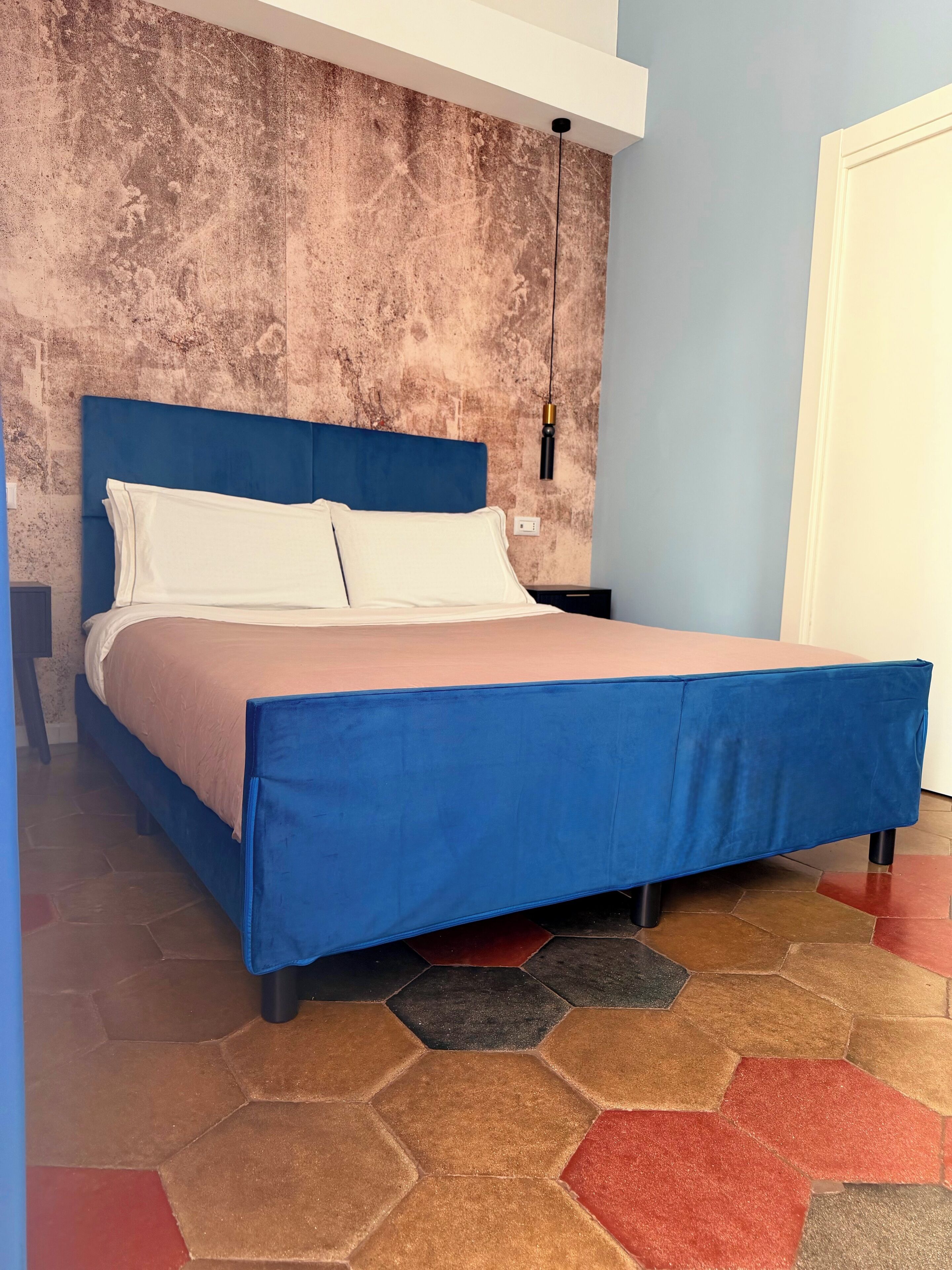 Un lit avec une tête de lit bleue, des oreillers blancs et une couvre-lit rose.