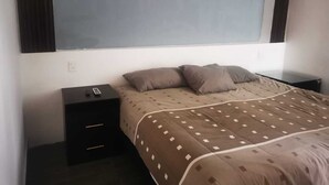 A bedroom with a bed, two bedside tables, a wall-mounted TV, and a power outlet. - ROOMS & SUITES (Monterrey)