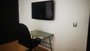 A small office space with a desk, a chair, and a mounted flat-screen TV. - ROOMS & SUITES (Monterrey)