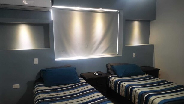 A bedroom with two single beds, a window with blinds, and a ceiling-mounted air conditioning unit. - ROOMS & SUITES (Monterrey)