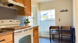 Una cocina con armarios de madera, estufa y comedor con sillas.