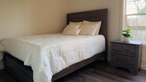 Un dormitorio con cama, mesita de noche y ventana.