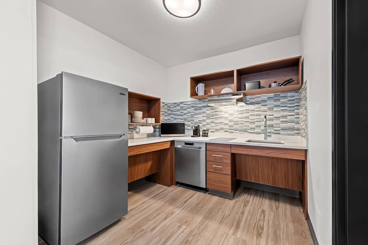 A modern kitchen with a stainless steel refrigerator, wooden cabinets, a microwave, and a dishwasher.