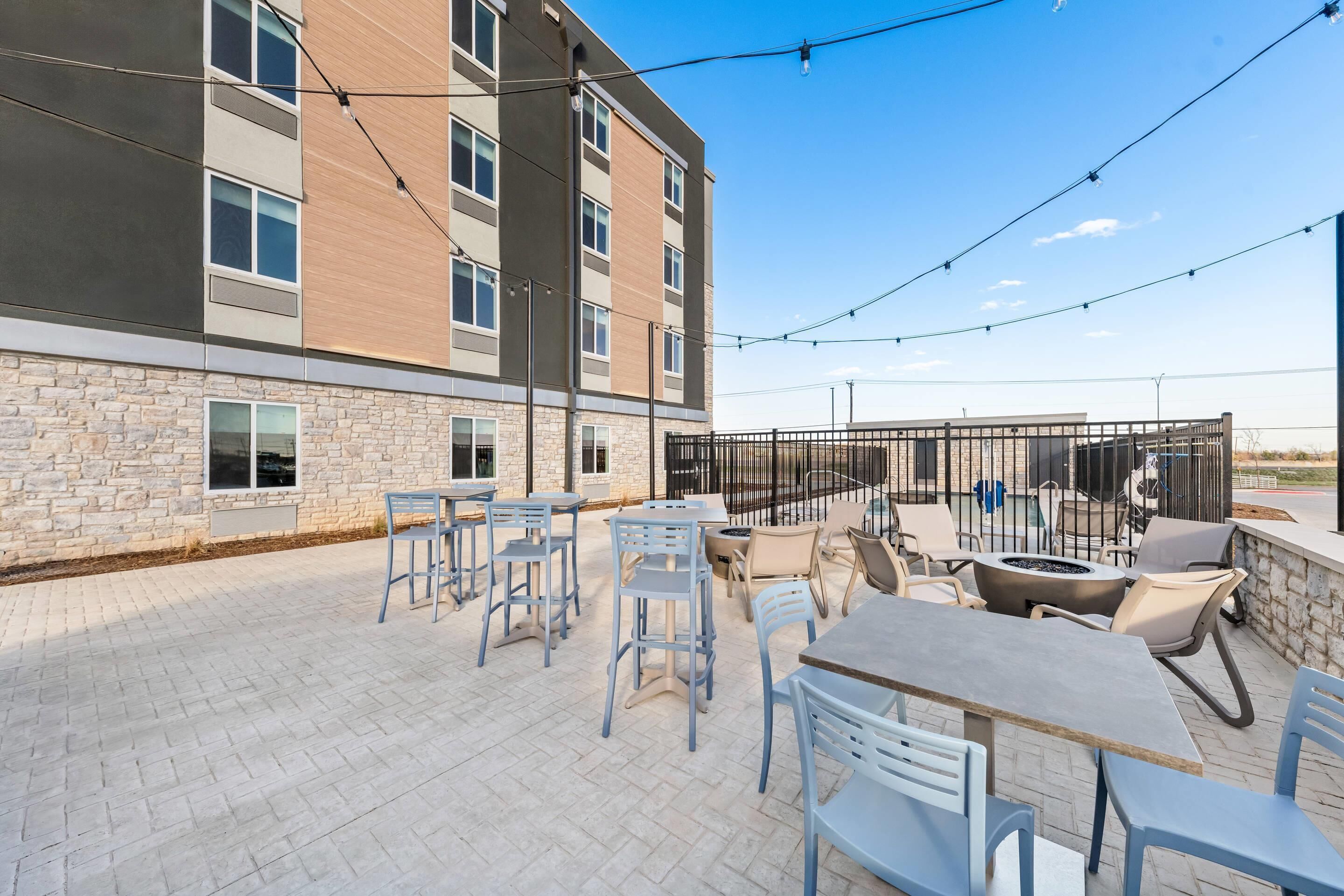 Un espace extérieur aménagé en terrasse, avec des tables et des chaises, un foyer et une vue sur un bâtiment à la façade en pierre.