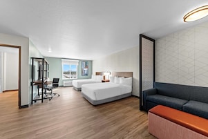 Una habitación de hotel moderna con una cama grande, un sofá, un escritorio con una silla y vistas al exterior.