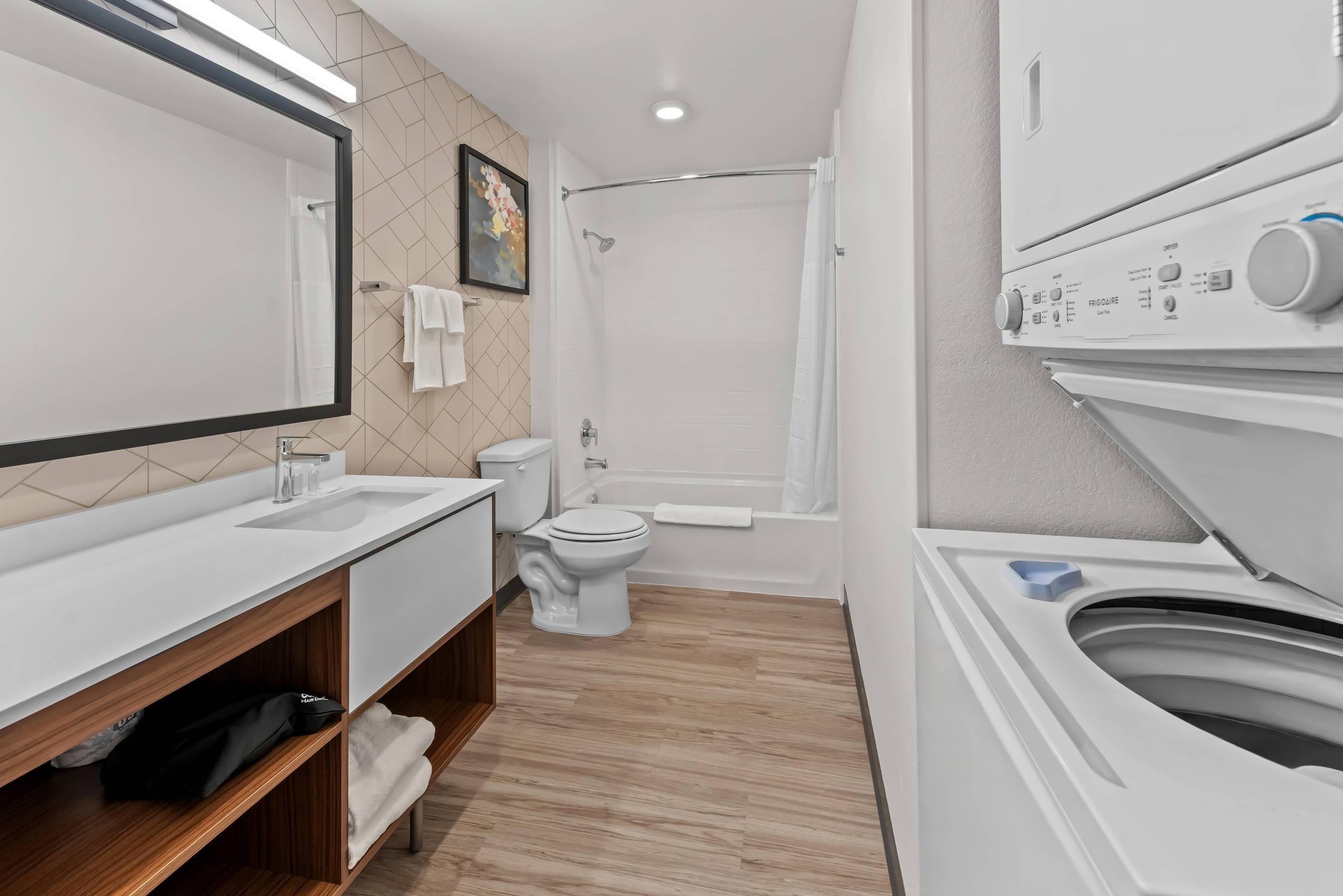 A modern bathroom with a large mirror, white sink, toilet, and shower.