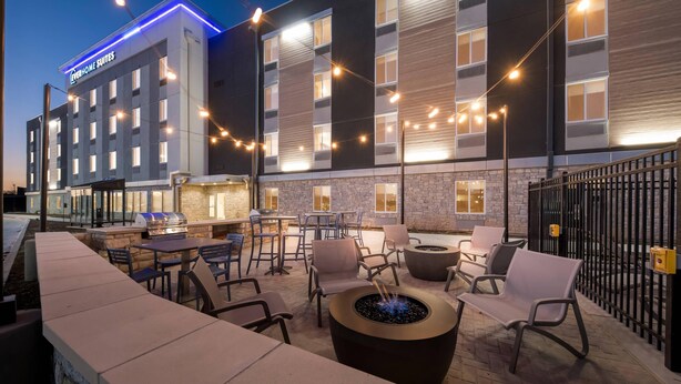 A hotel exterior with outdoor seating, a fire pit, and string lights. - Everhome Suites Waco by Choice Hotels (Waco)