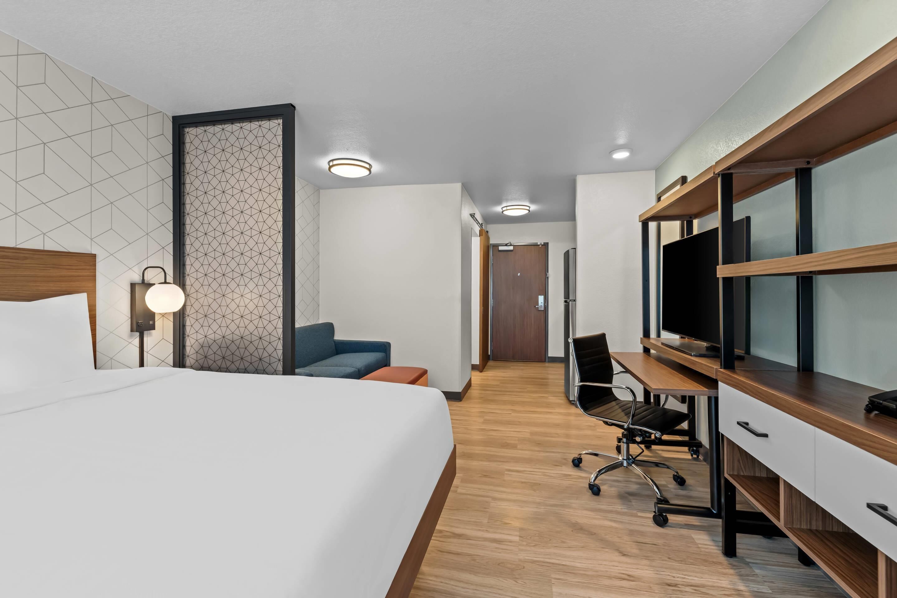 Ein modernes Hotelzimmer mit einem großen Bett, einem Schreibtisch mit Computer und einem Fernseher.