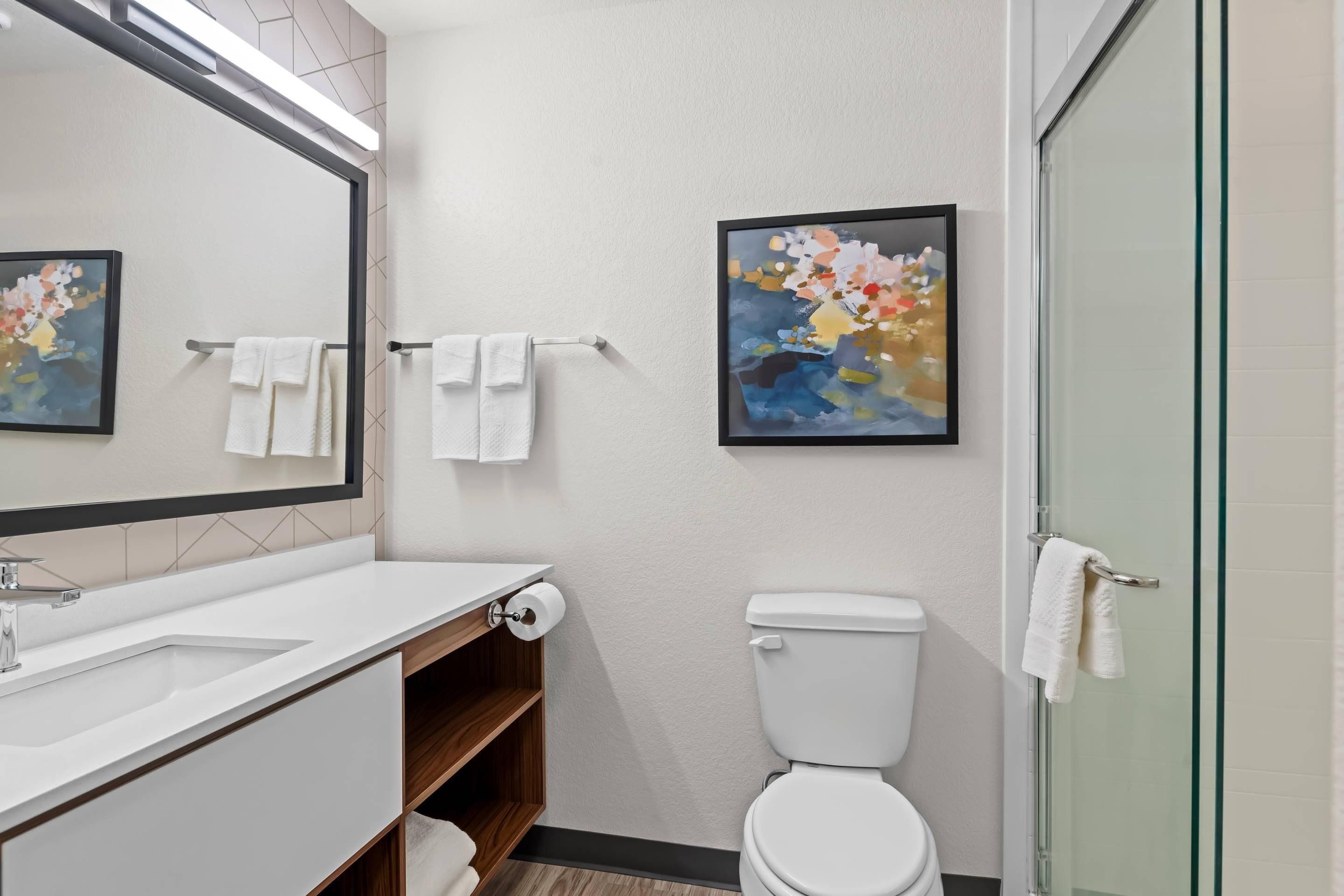 A modern bathroom with a white sink, mirror, toilet, and glass shower enclosure.