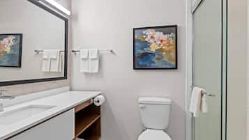 A modern bathroom with a white sink, mirror, toilet, and glass shower enclosure.