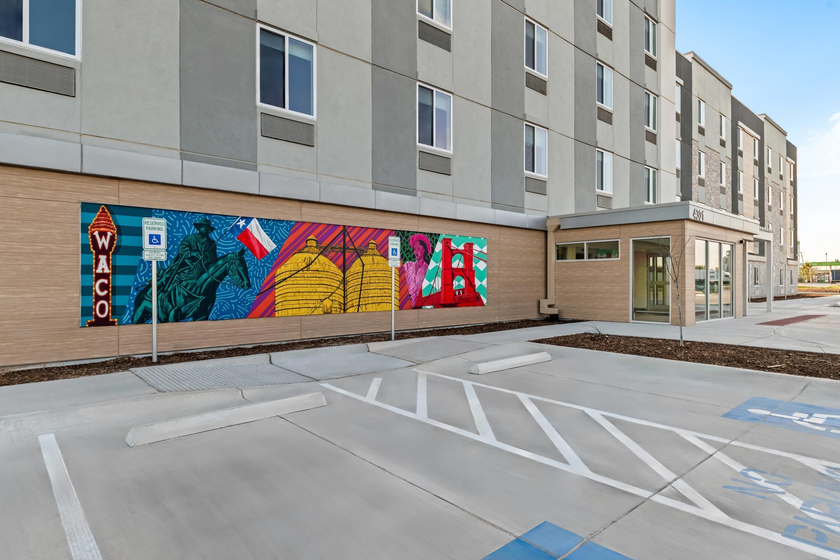 A modern building with a colorful mural on the side, a wheelchair-accessible ramp, and a clear view of the entrance.