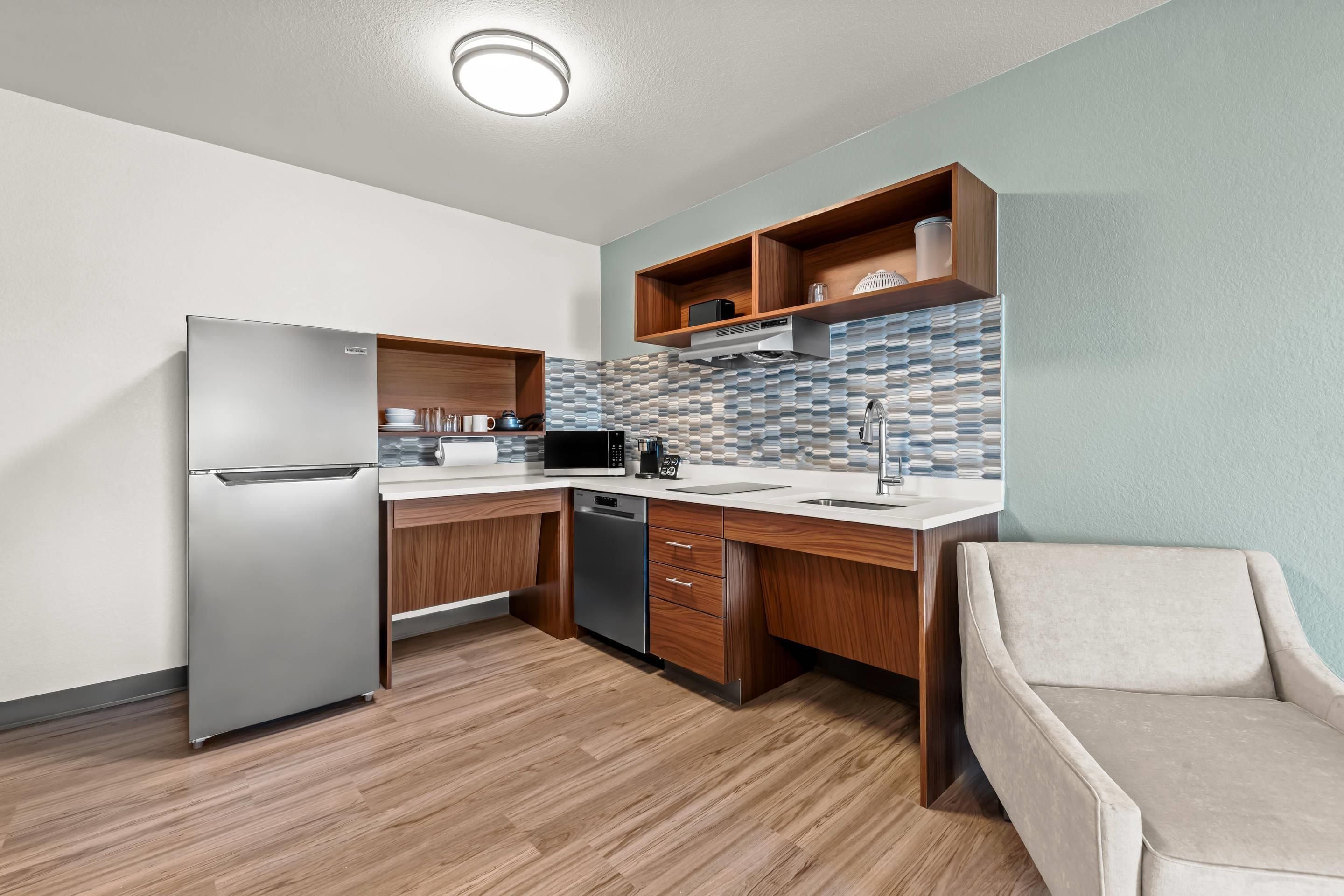 A modern kitchen with a built-in refrigerator, microwave, and dishwasher, wooden cabinets, and a tiled backsplash.