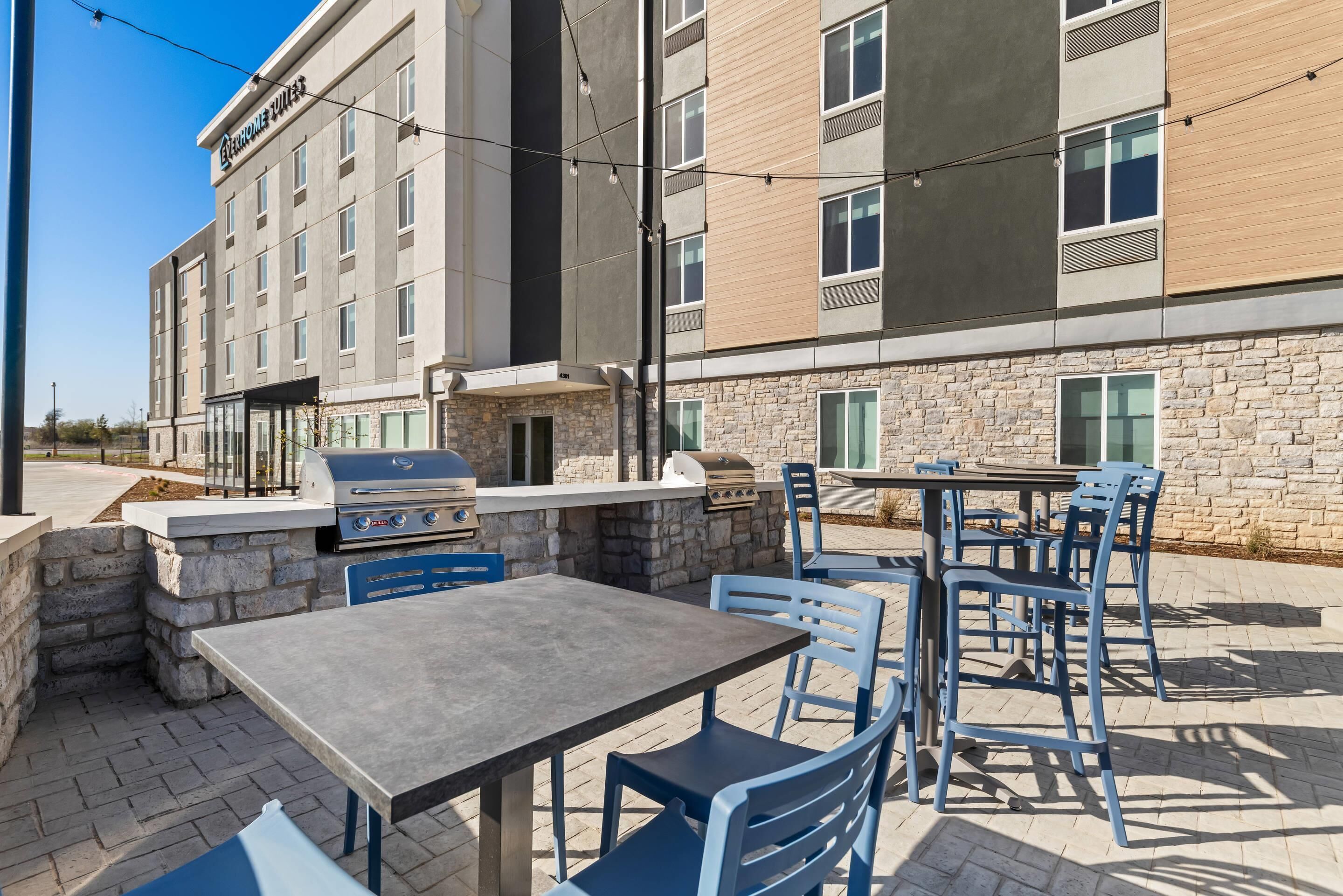 An outdoor patio with a barbecue grill, stone walls, and blue chairs.