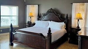 A spacious bedroom with a large bed, two bedside tables with lamps, a ceiling fan, and a window with blinds. - LAKE HOUSE. Serene, charming 5-bedroom house in greater New Orleans. (New Orleans)