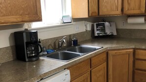 Una cucina con mobili in legno, lavastoviglie, macchina da caffè e una finestra che lascia entrare luce naturale.