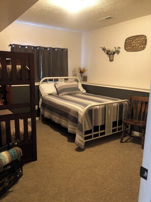 A bedroom with a bunk bed, a single bed, a chair, and a decorative wall piece.