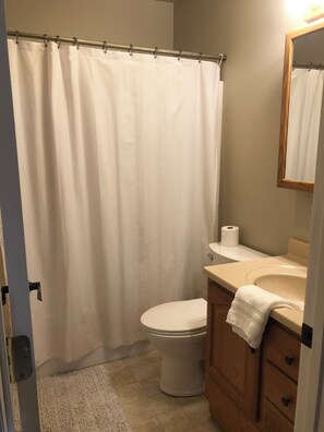 A bathroom with a shower curtain, toilet, sink, and a mirror.