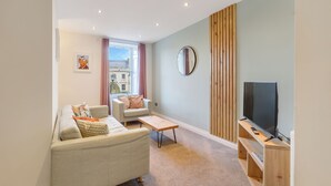 Una sala de estar moderna con sofá, sillón, mesa de centro y televisor sobre un mueble de madera.