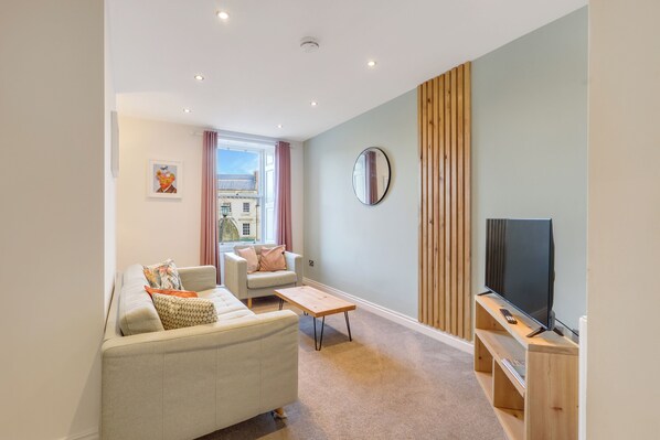 A modern living room with a sofa, armchair, coffee table, and TV on a wooden stand.