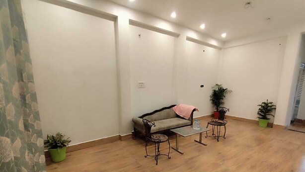 Una habitación amplia con suelo de madera, un sofá, dos mesitas y plantas en macetas.