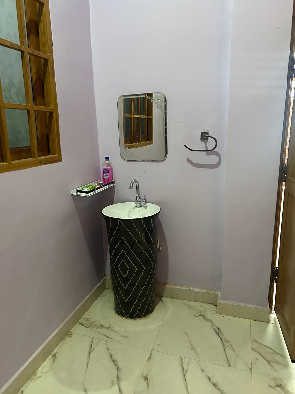 A bathroom with a pedestal sink, a small window with a wooden frame, a mirror, and a towel rack.