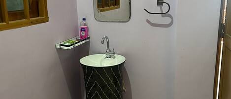 A bathroom with a pedestal sink, a small window with a wooden frame, a mirror, and a towel rack.