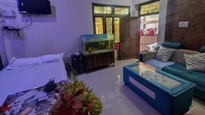 Una sala de estar con sofá, televisor, acuario y puerta que da a otra habitación.
