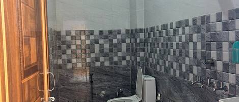 A bathroom with a toilet, a shower, and a green bucket.