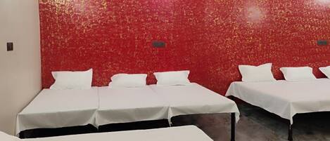 Una stanza con tre letti, una ventola a soffitto e un muro con un motivo rosso.