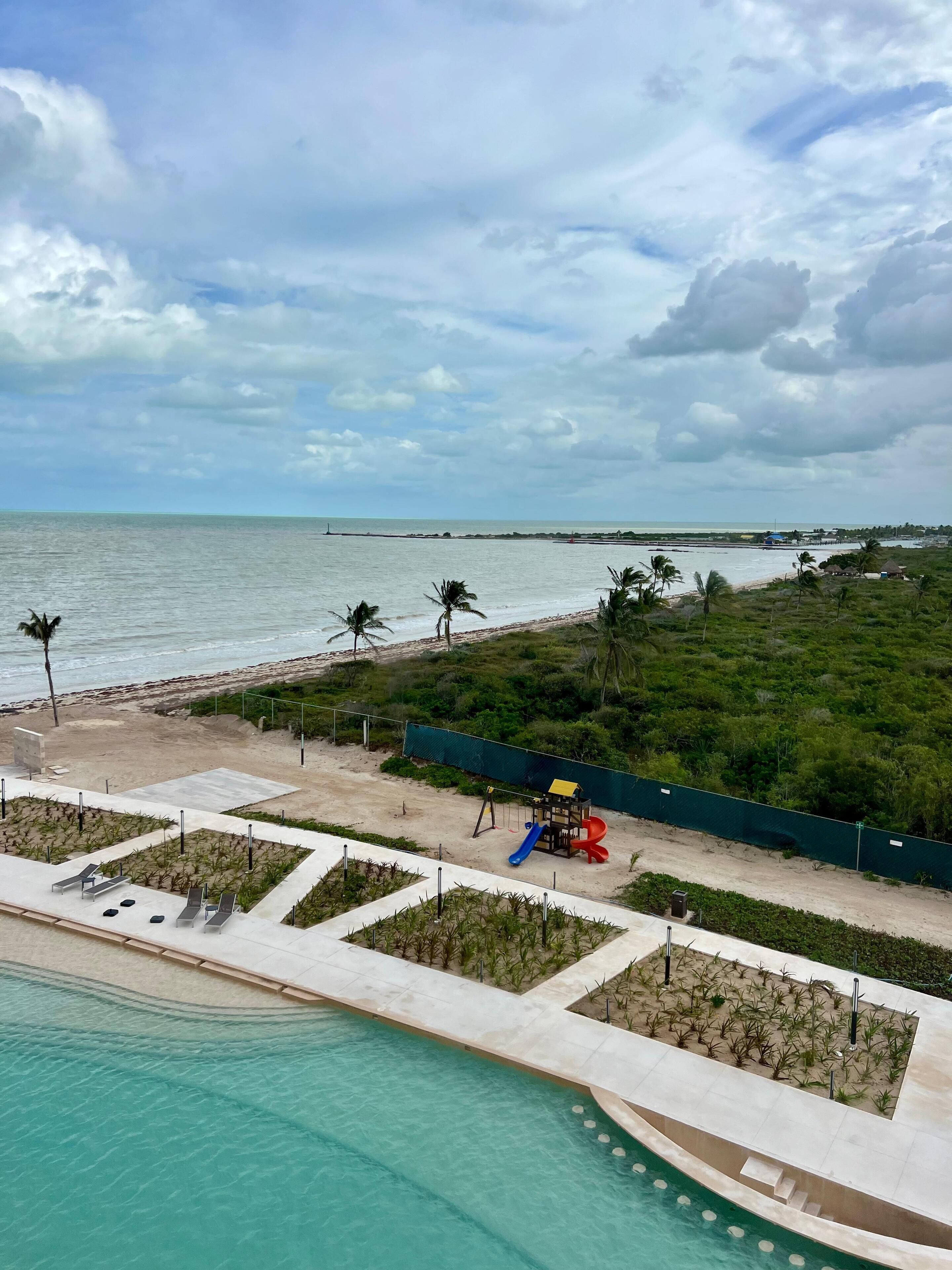 A beach view with a pool, palm trees, and a playground.