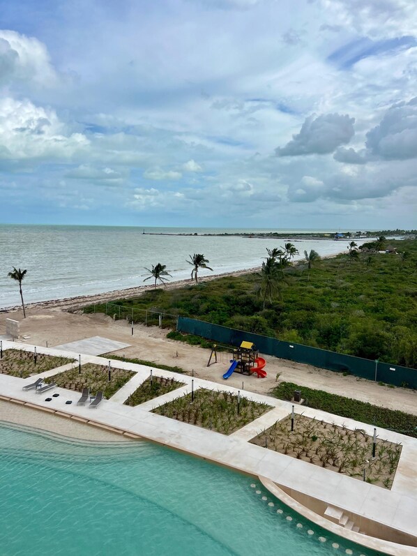 A beach view with a pool, palm trees, and a playground. - Penthouse Navela 405, by Cercana (Telchac Puerto)