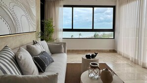 Un soggiorno moderno con una grande finestra, una ventola a soffitto, un divano con cuscini a righe e un tavolino rotondo con oggetti decorativi.