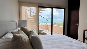 Una camera d'albergo con un letto, un comodino, una lampada e vista su un balcone con ringhiera.