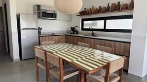 Een moderne keuken met een houten tafel en stoelen, een inbouwoven, magnetron en een hanglamp.