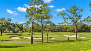 Campo de golf con búnkeres de arena, árboles y un cielo azul despejado.